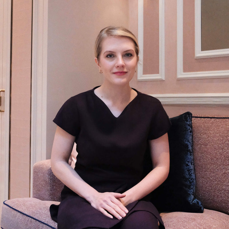Justyna sitting on a couch in our elegant executive facial treatment room with decorative wall molding.