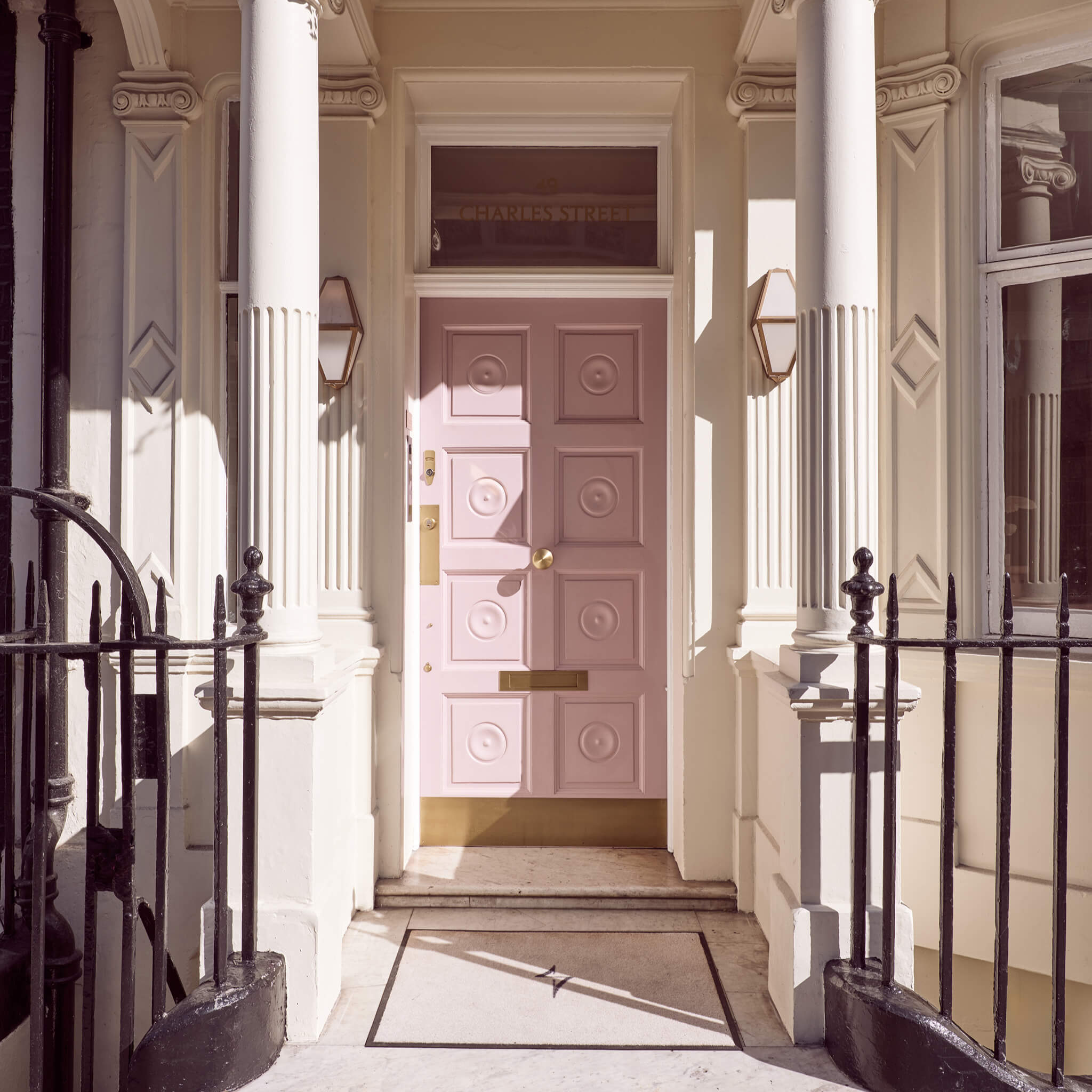 The cinder rose door with decorative patterns on the facade of Le Petit Saint in Mayfair London with columns and black metal gate.