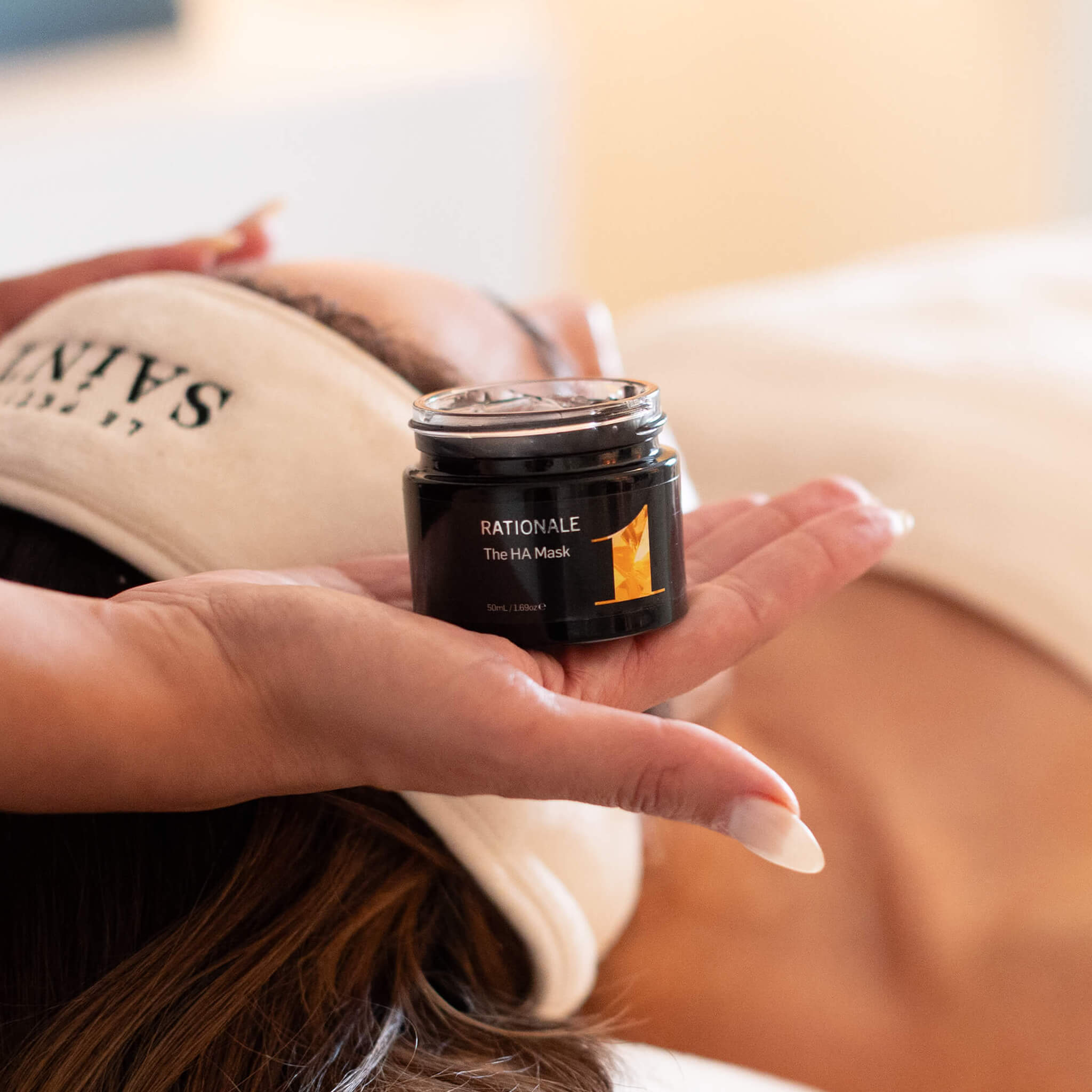 A dermal therapist's hand holding the Professional Advanced Rationale range. She applies the Rationale H.A. mask on the patient's face who is enjoying our signature Rationale Facial. 