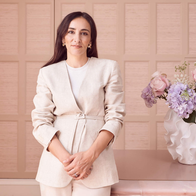 Rita our Clinic Manager in a beige suit standing in front of the reception desk at Le Petit Saint with a vase of flowers.