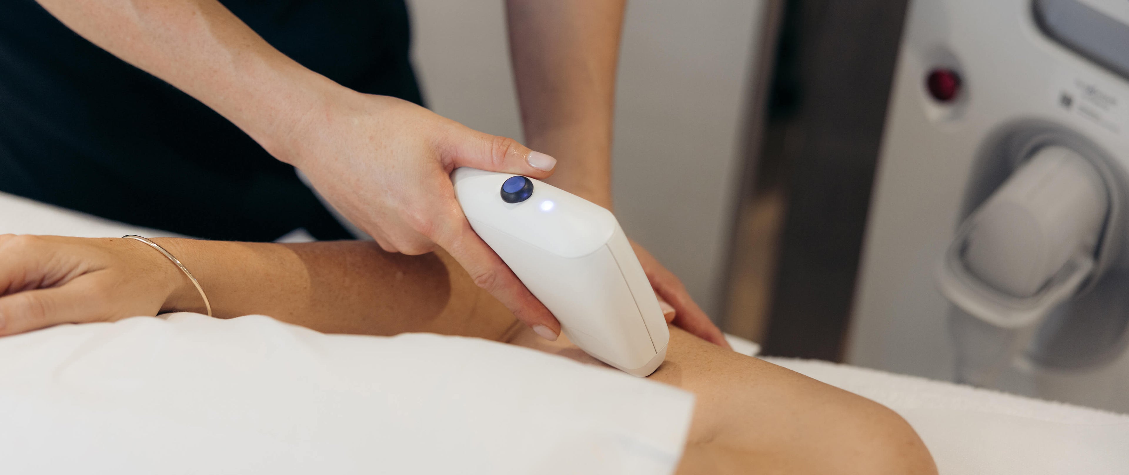 Dermal therapist using a handheld sofwave device on a patient's arm in a medical setting.